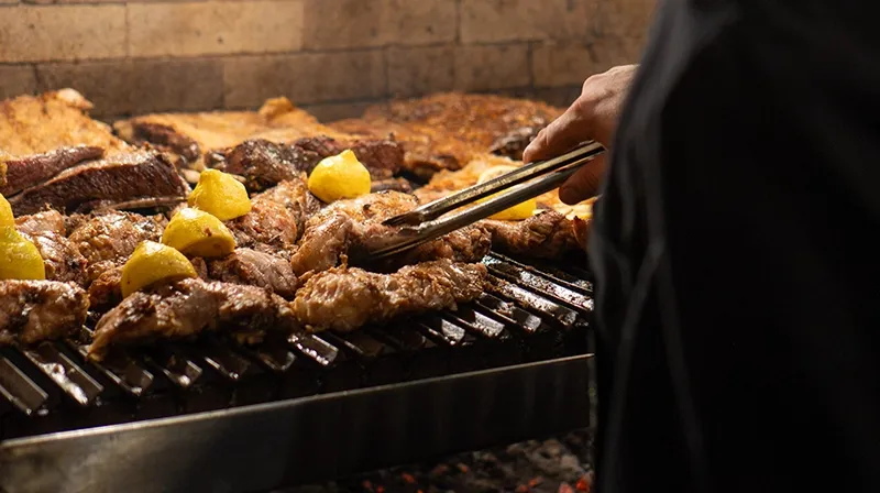 Cortes de carne con limón dorándose en la parrilla, dados vuelta con pinza