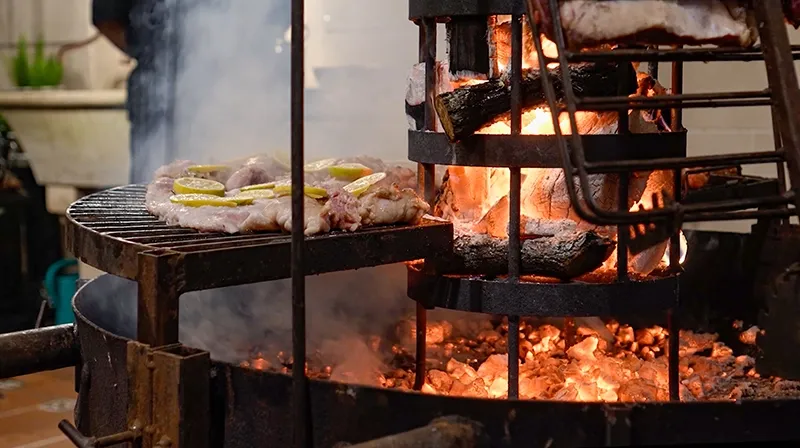 Brasero de leña encendido junto a la grilla con carne y rodajas de limón