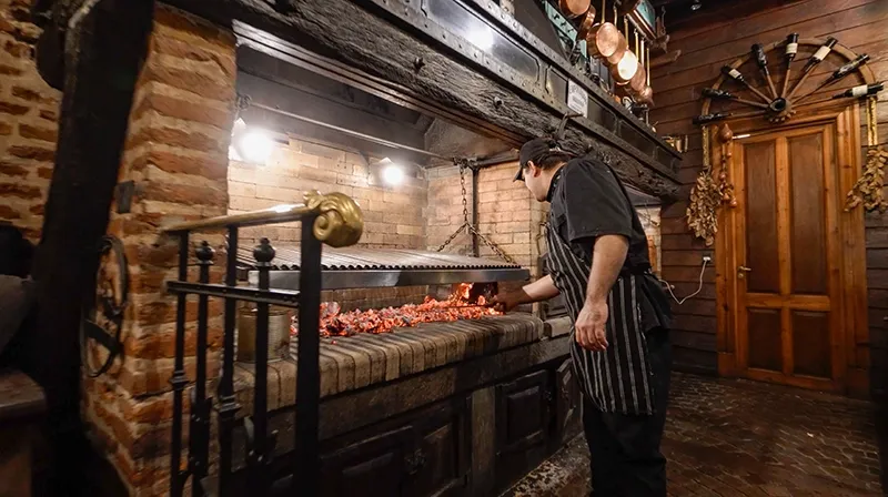 Asador frente a la parrilla de ladrillo del quincho, con las brasas encendidas