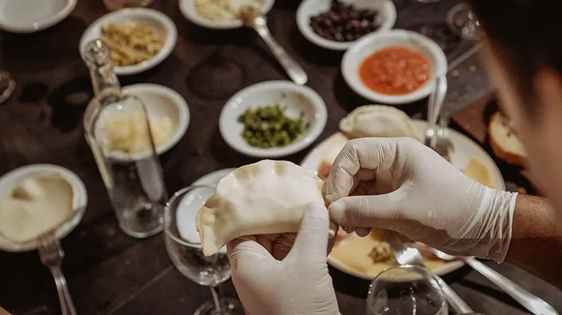 Empanada recién armada sobre la mesa, entre cuencos con rellenos y condimentos