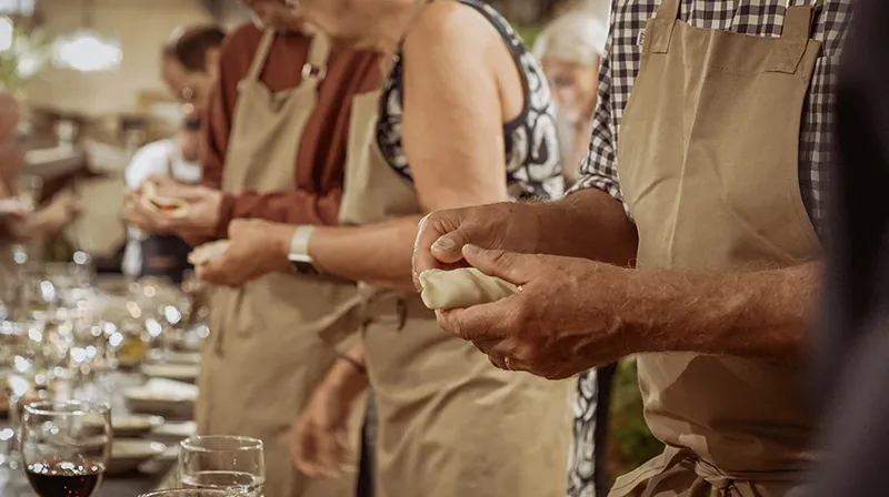 Invitados con delantal cerrando empanadas junto a la mesa servida