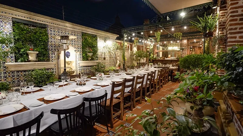 Patio de noche con la mesa larga preparada, azulejos y vegetación
