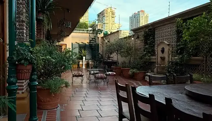 Pátio colonial do RoofTop San Telmo com plantas, galeria e mesas de madeira